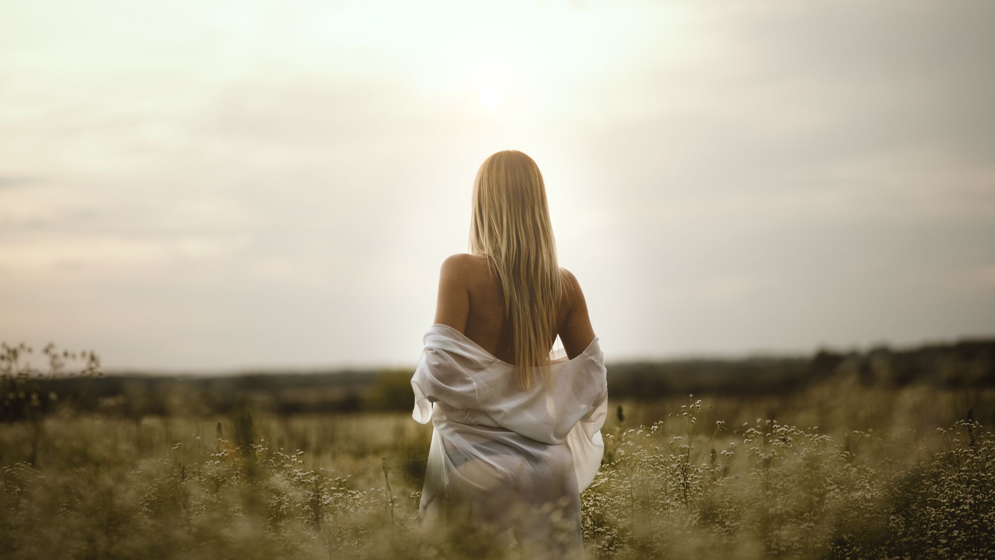 Blondynka w białej koszuli na łące, widok od tyłu